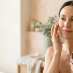 Donna che applica un siero viso sulla guancia con i polpastrelli, luce naturale del mattino